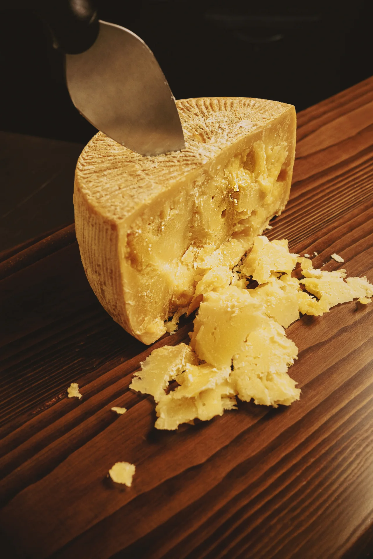 A wheel of aged cheese being cut on a wooden counter