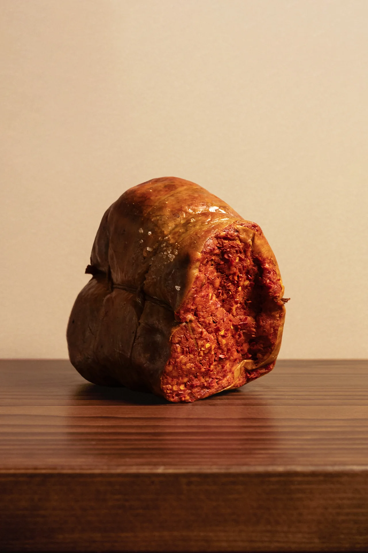 A whole artisanal salame on a wooden counter